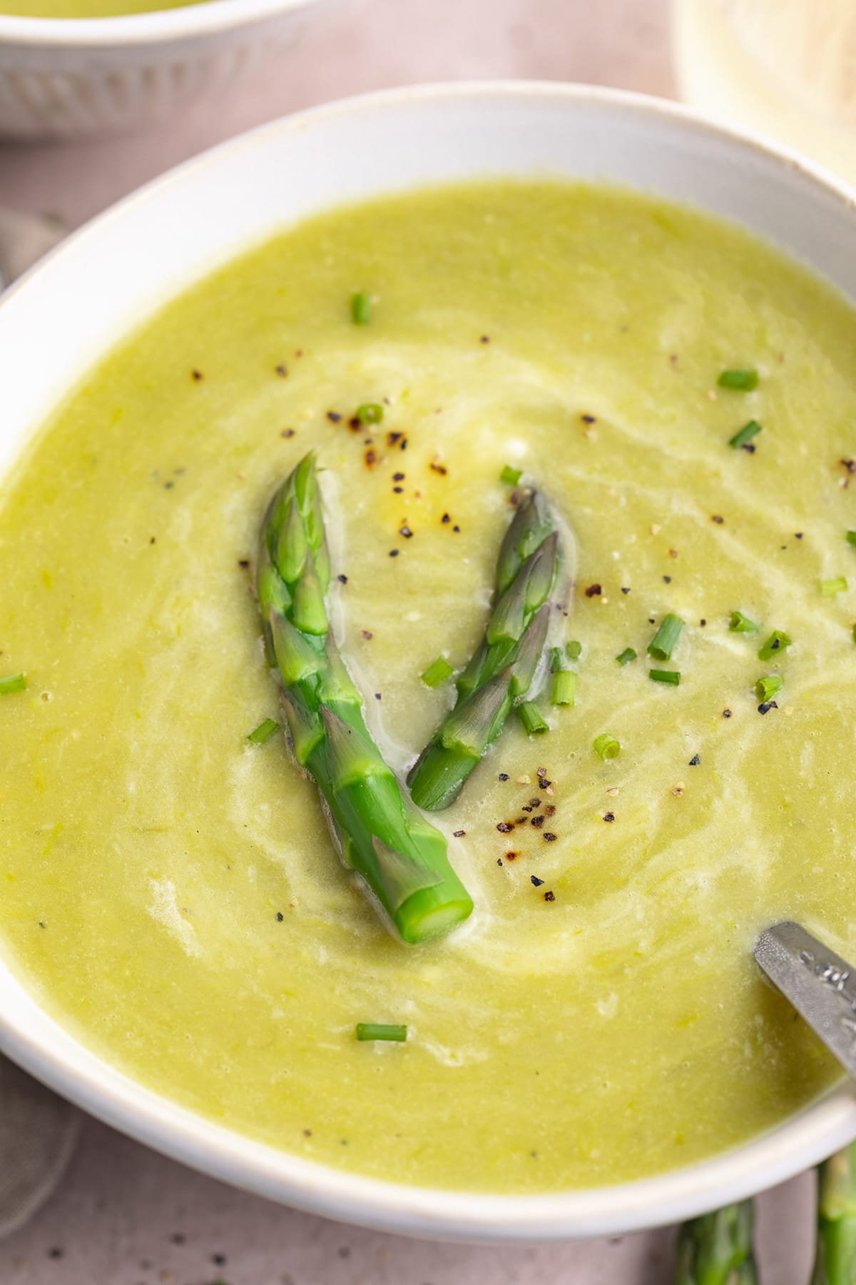 Close-up, angled view of a white bowl of potato asparagus soup garnished with asparagus.
