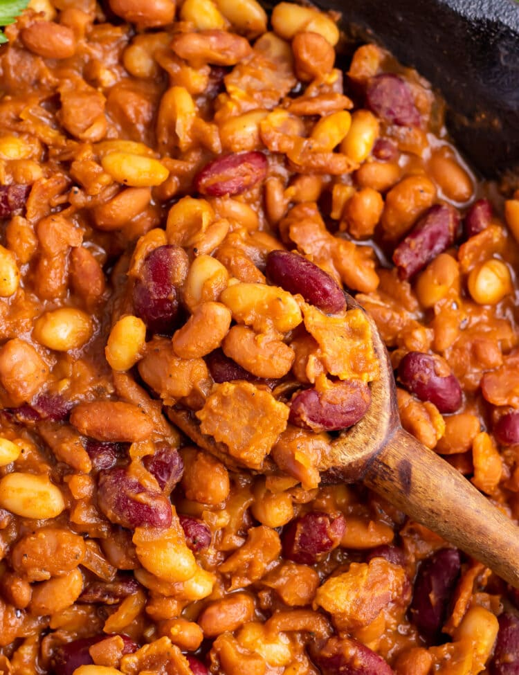Close-up of smoked baked beans in a large cast-iron skillet with a large wooden spoon.