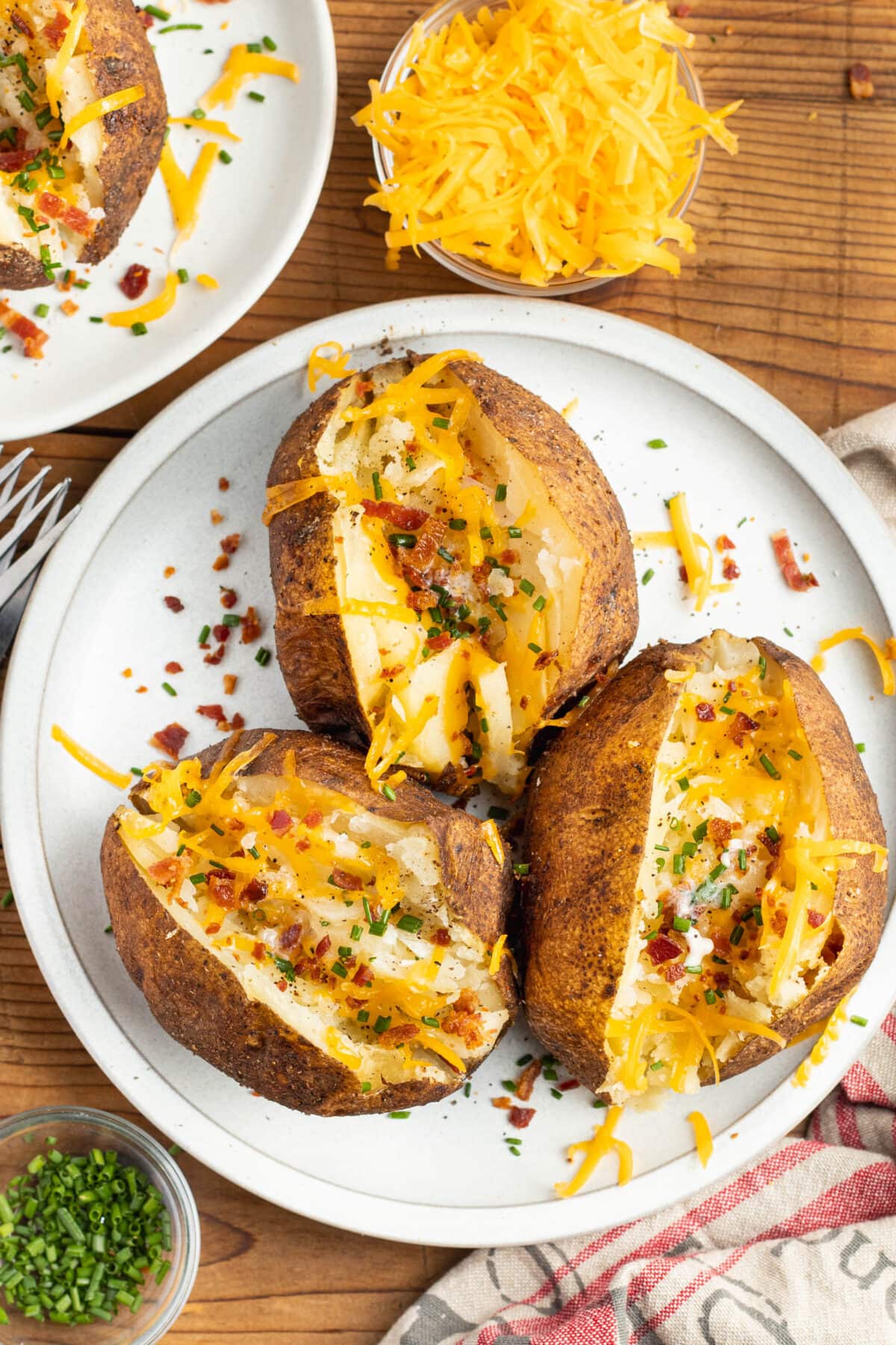 Three smoked baked potatoes sliced open and topped with cheese and bacon, arranged on a white plate.