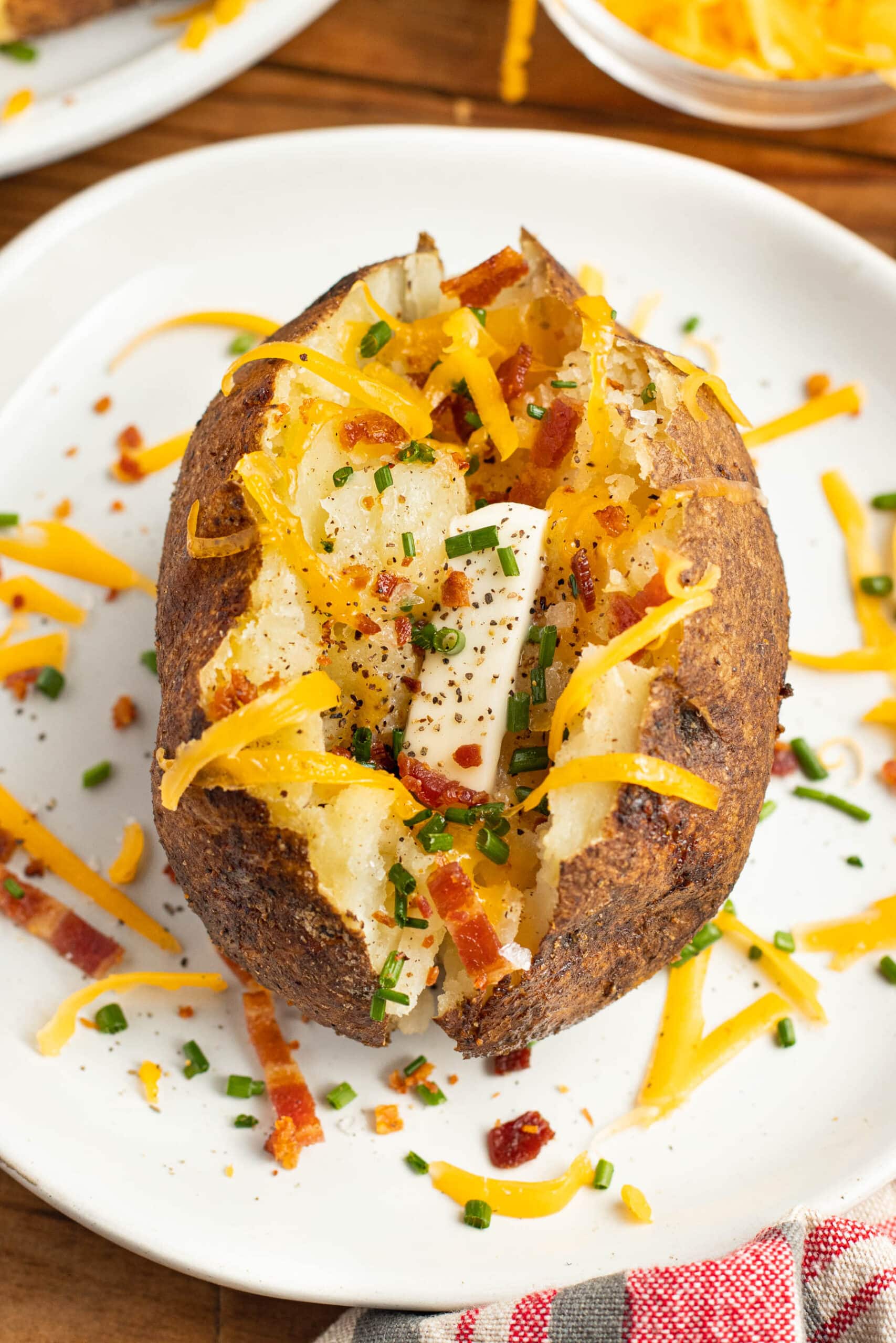 Overhead view of a smoked baked potato topped with cheese and bacon on a white plate.