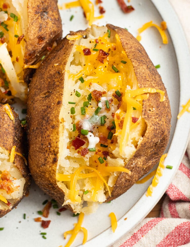 Overhead view of a smoked baked potato topped with cheese and bacon on a white plate.