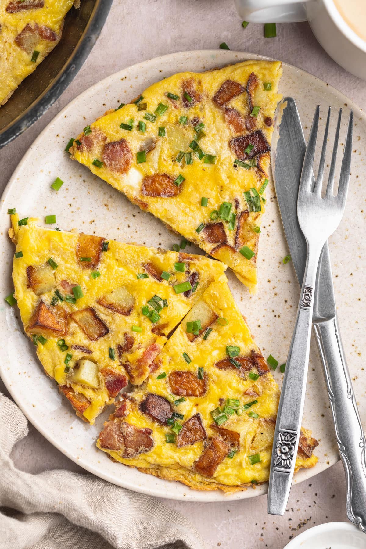 A country omelette, sliced into triangular wedges, on a plate with a fork and knife.