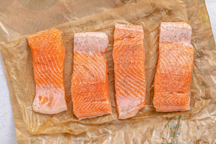 Salmon slices on parchment paper with salt and pepper.