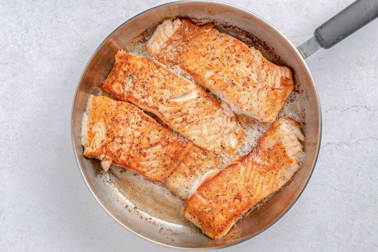 Salmon slices in a large skillet with melted butter.