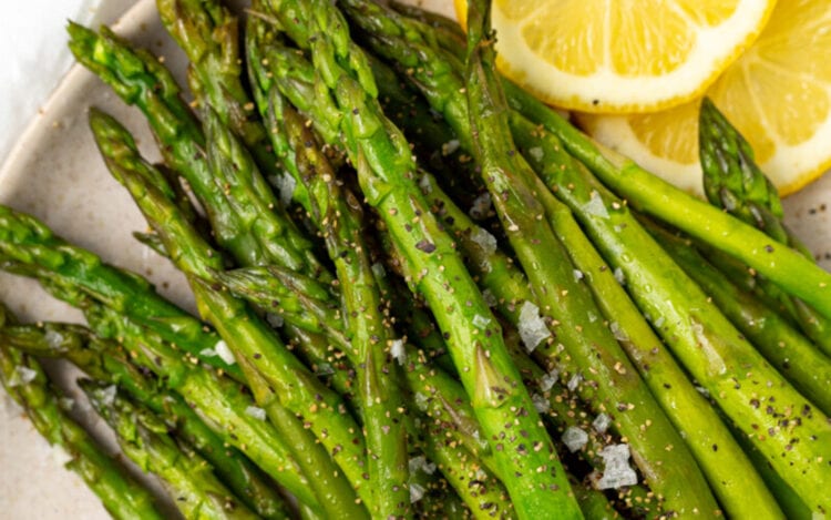 Bright green Instant Pot asparagus on a white plate with lemon slices.