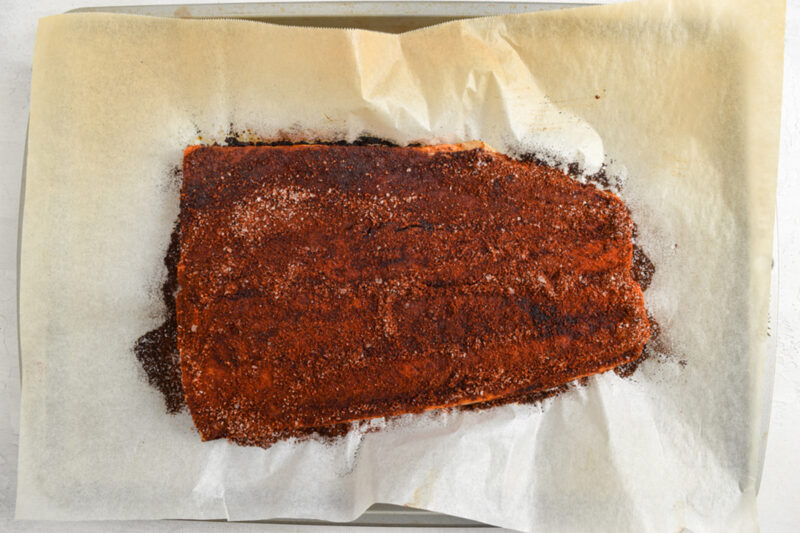 Seasoned salmon fillet on a baking sheet lined with parchment paper.