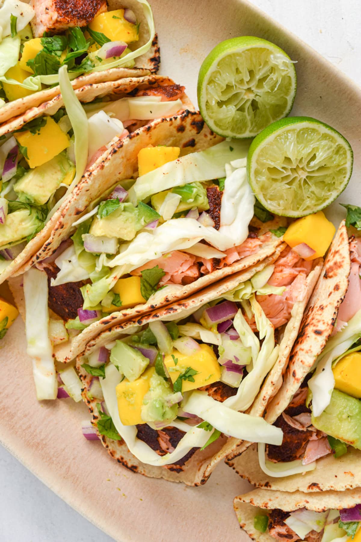 4 salmon tacos topped with slaw and mango salsa on an oval platter.