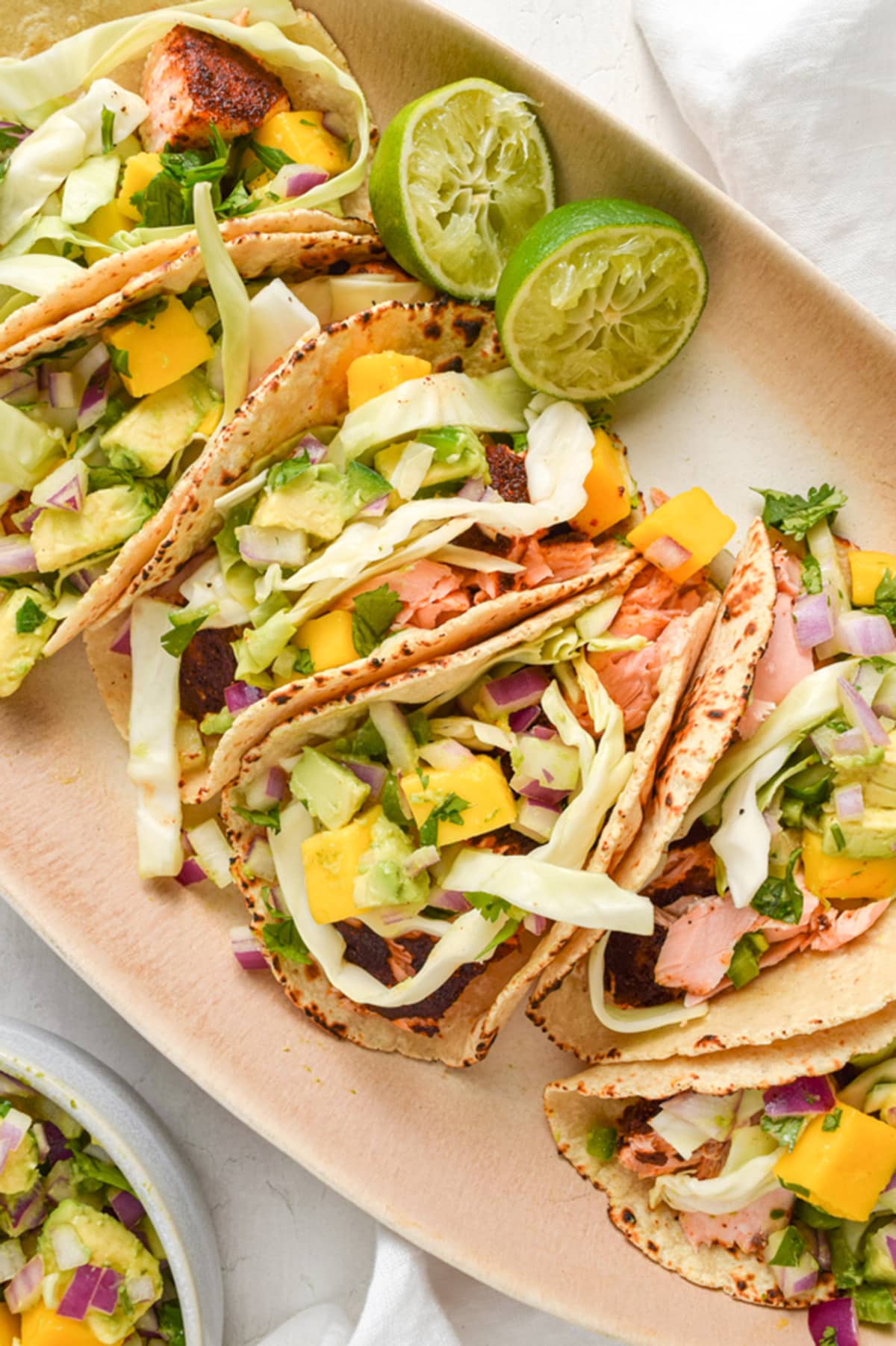 4 salmon tacos topped with slaw and mango salsa on an oval platter.