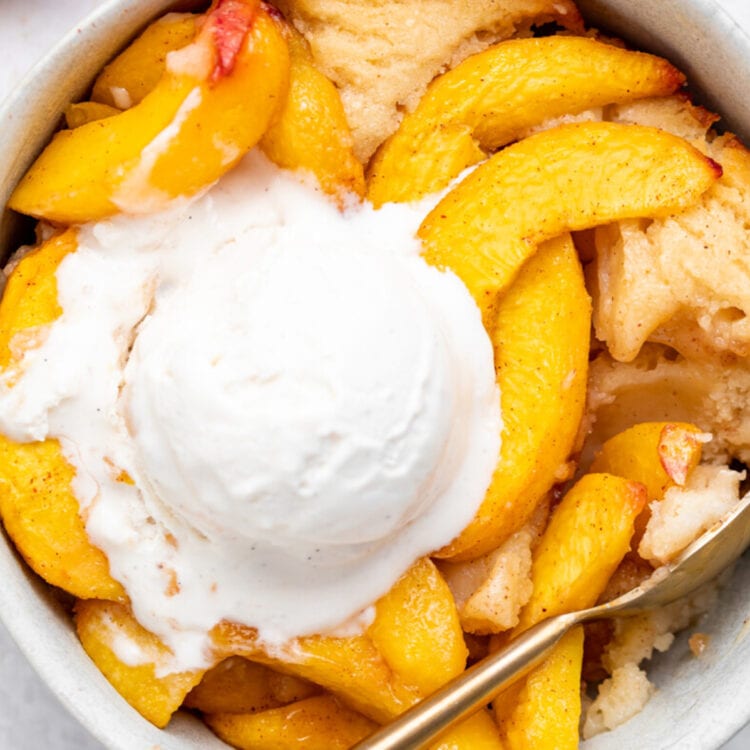 Vegan peach cobbler in a bowl with a scoop of vegan vanilla ice cream.