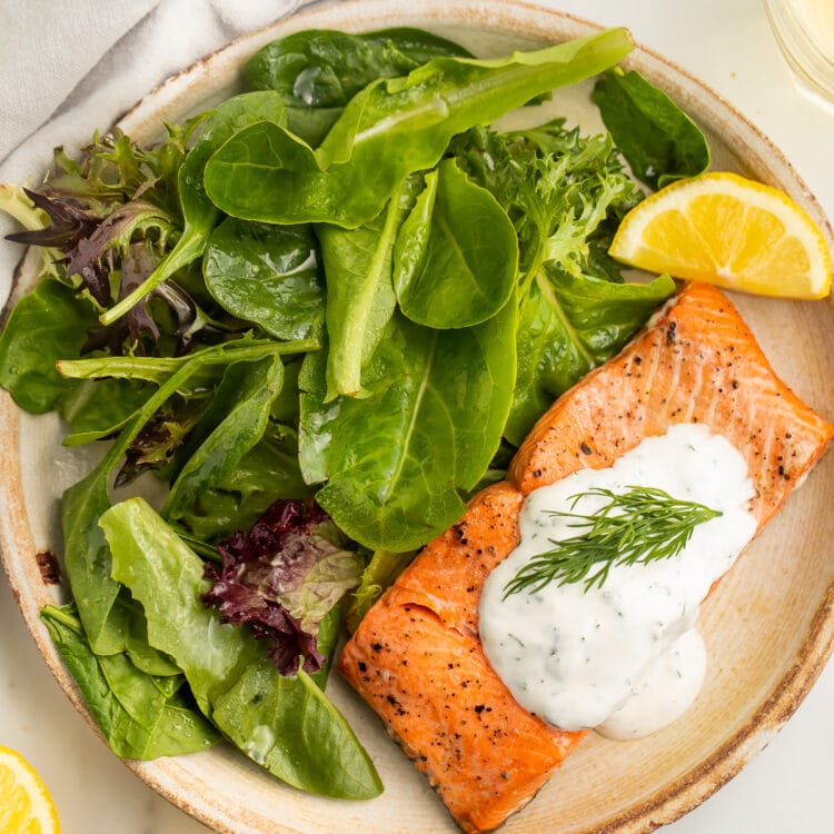 A salmon fillet, cooked in the air fryer, plated with a small green salad and a dollop of creamy dill sauce.