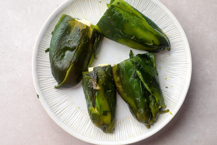 Charred poblano peppers stuffed with Monterey jack on a white plate.