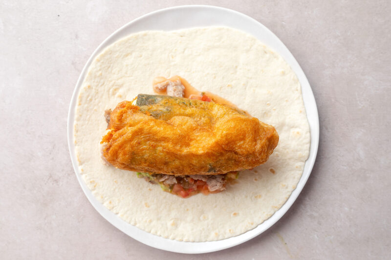 Unrolled chile relleno burrito with a chile rellano on top.