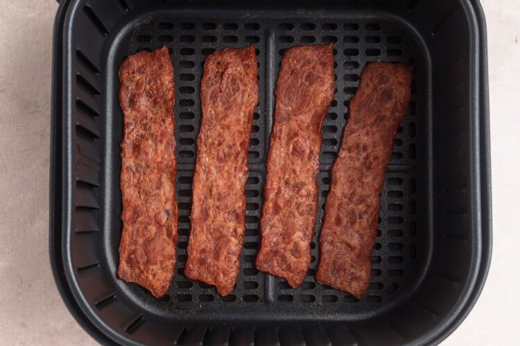 Strips of turkey bacon in air fryer basket.