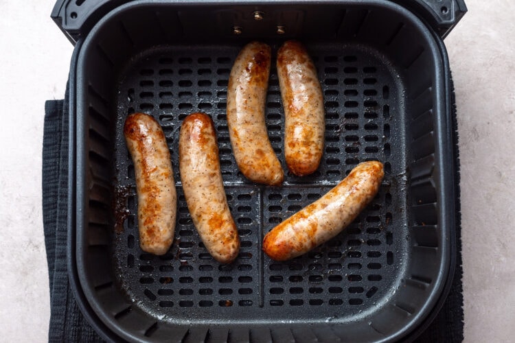 5 cooked Italian sausages in an air fryer basket.