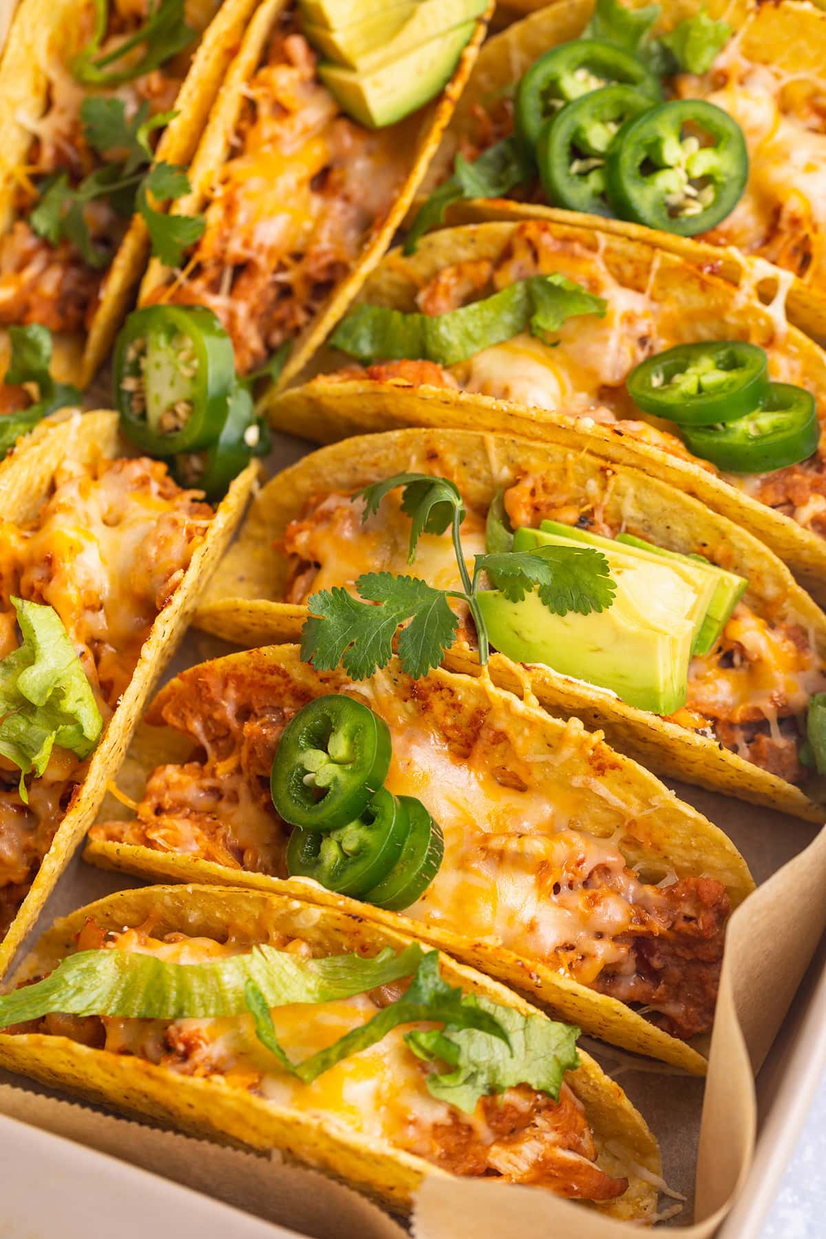 Overhead, close-up view of several baked chicken tacos in crunchy shells with avocados and jalapenos on top.