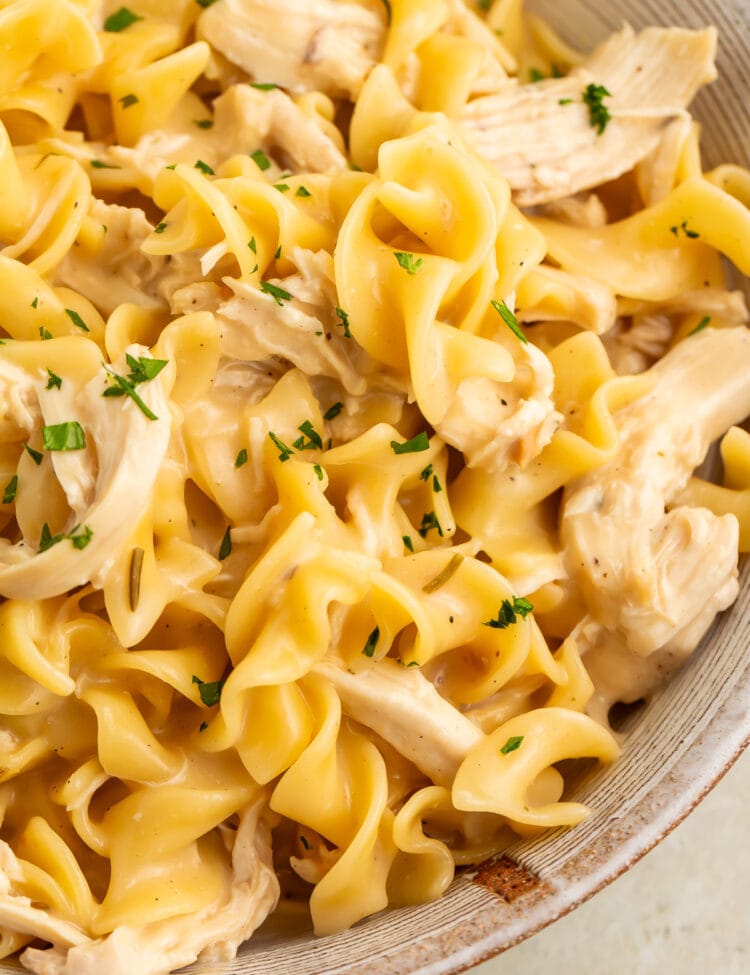 Instant Pot chicken and noodles in a large white bowl, shot close-up to show the chunks of chicken and twisty noodles.