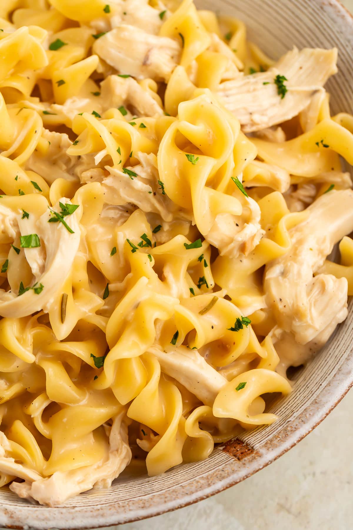 Instant Pot chicken and noodles in a large white bowl, shot close-up to show the chunks of chicken and twisty noodles.