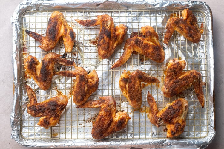 Seasoned whole chicken wings on a large baking sheet lined with foil and topped with a baking rack.