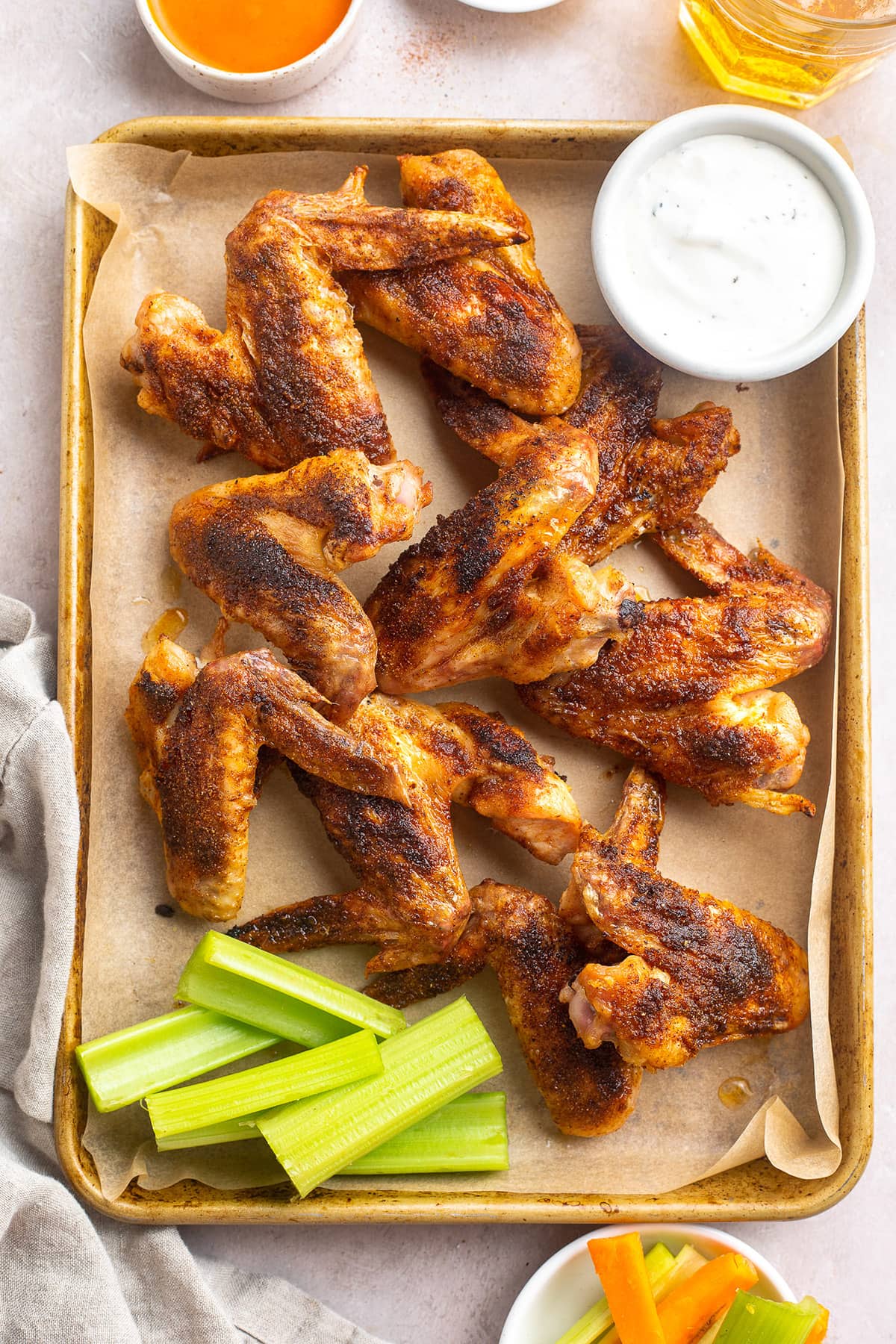 Whole chicken wings on a baking sheet lined with parchment paper next to a ramekin of ranch dressing.