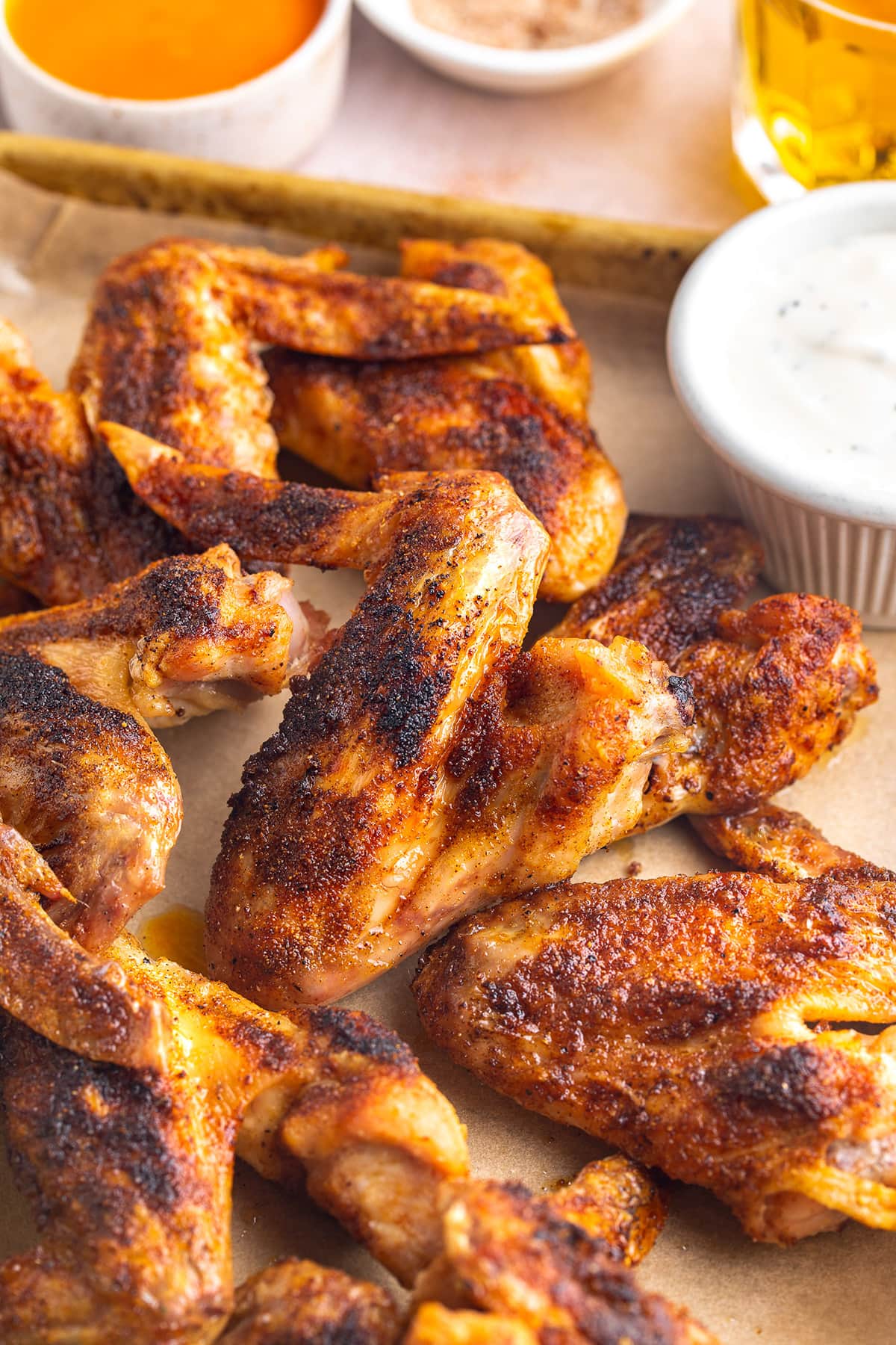 Whole chicken wings on a baking sheet lined with parchment paper next to a ramekin of ranch dressing.