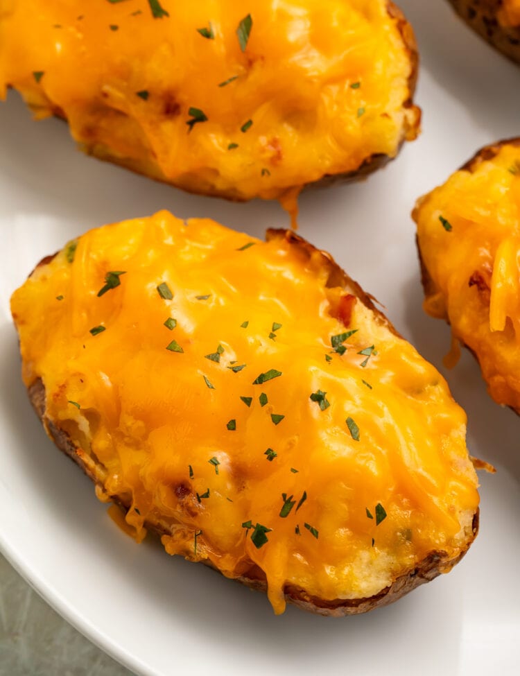 Air fryer twice baked potatoes topped with melty cheddar cheese and a garnish of chives on a white plate.