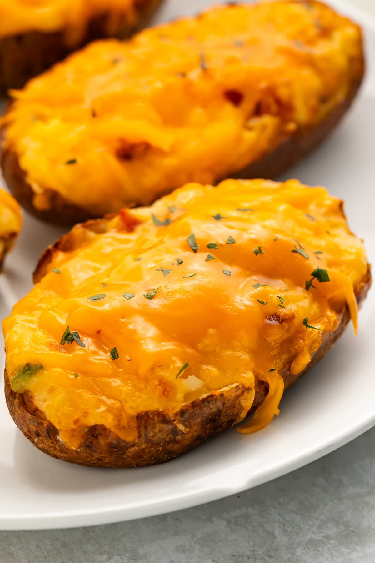 Air fryer twice baked potatoes topped with melty cheddar cheese and a garnish of chives on a white plate.