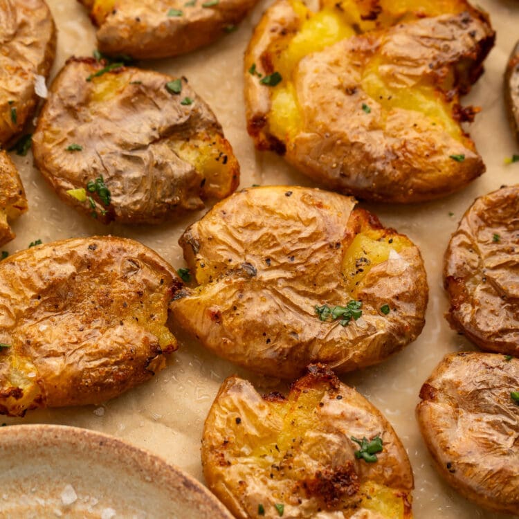 Multiple smashed potatoes, cooked in the air fryer, arranged on a sheet of parchment paper next to a small dish of salt.