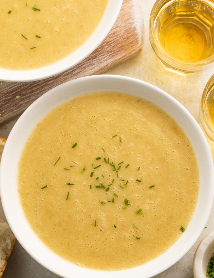 Bowls of yellow, creamy potato leek soup cooked in an Instant Pot on a table top with pieces of crusty bread surrounding.