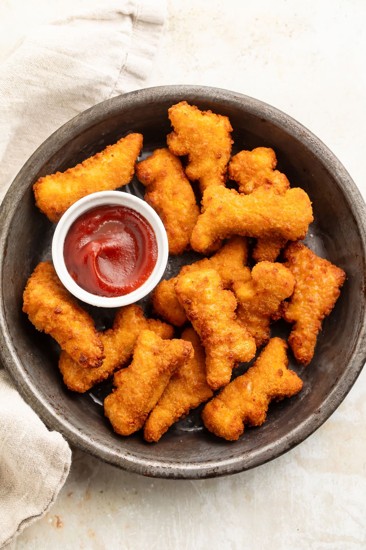 Air fryer dino nuggets on a plate with a small ramekin of ketchup.