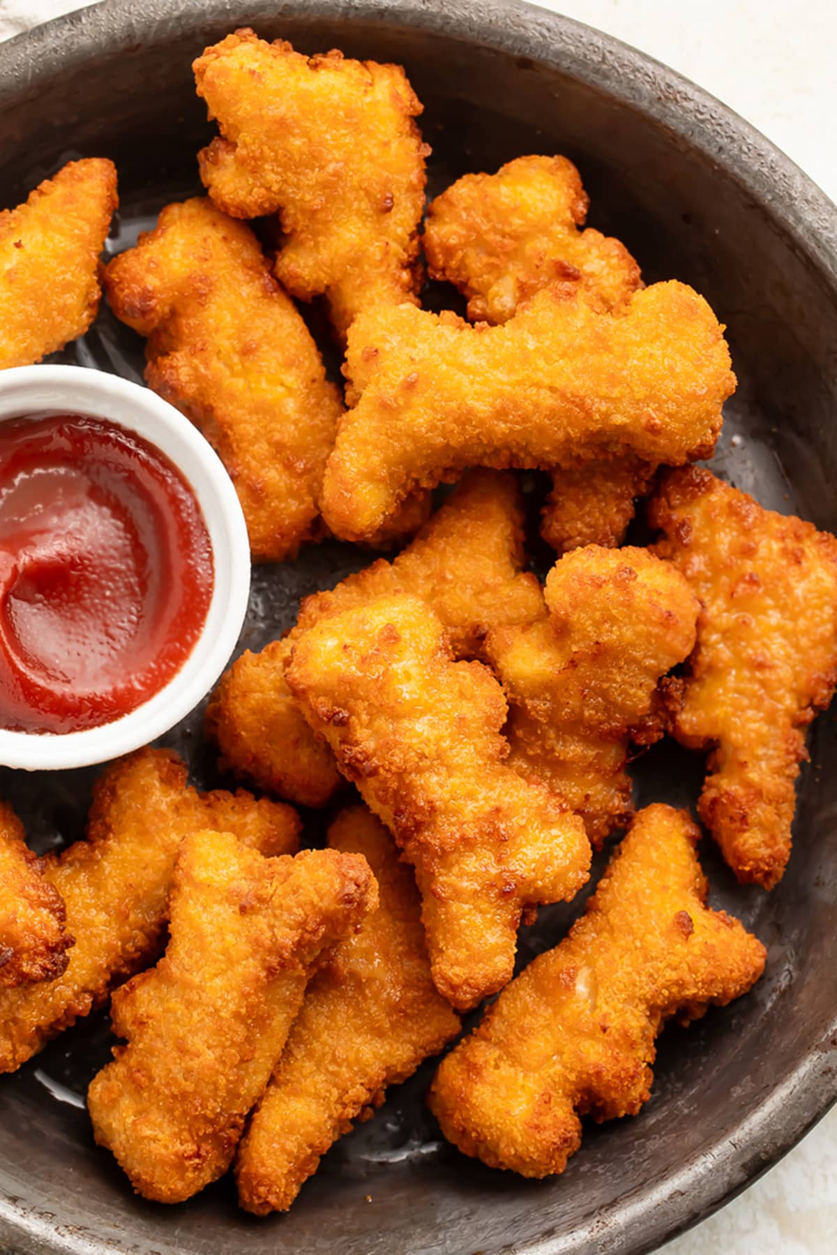 Air fryer dino nuggets on a plate with a small ramekin of ketchup.