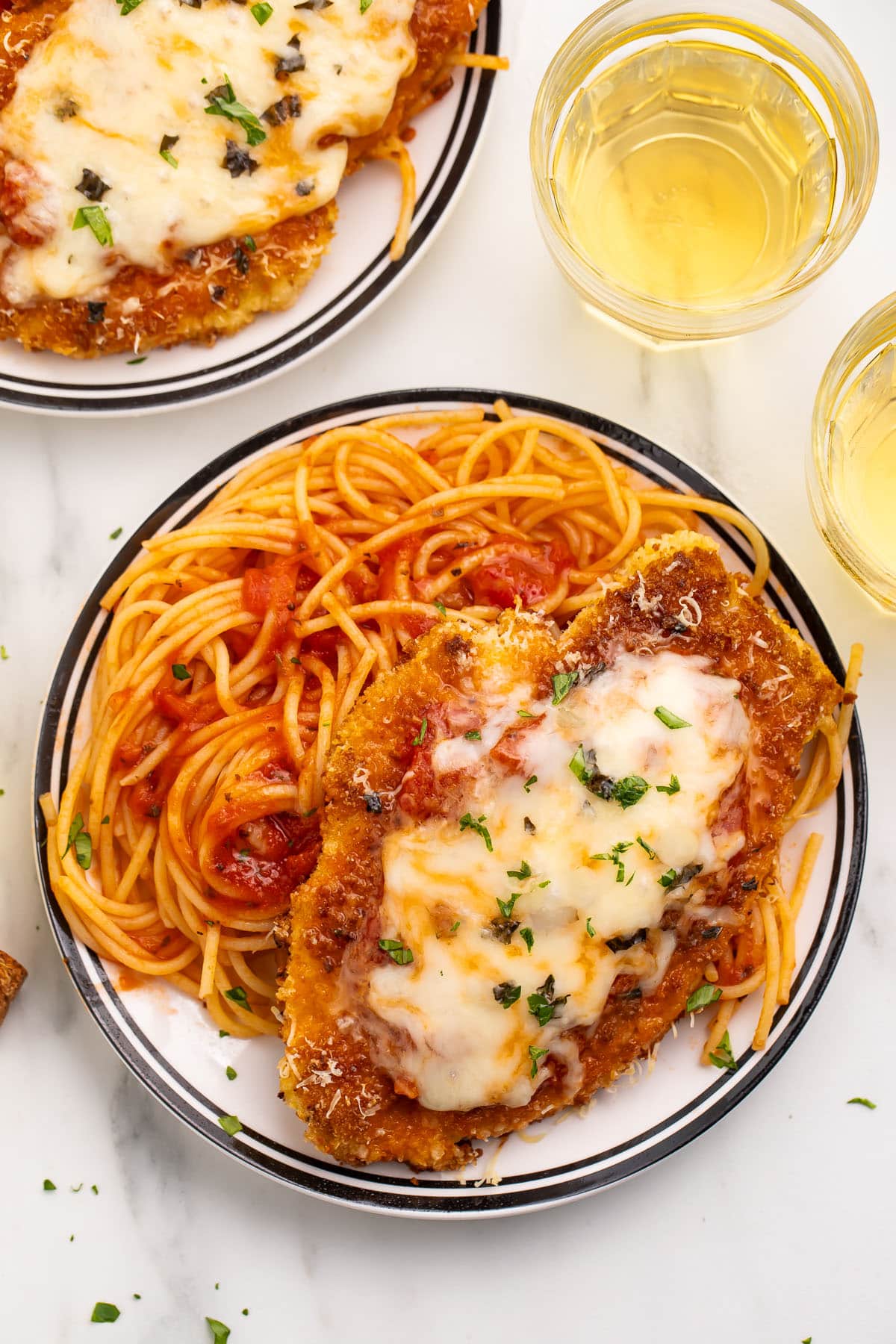 Gluten free chicken parmesan on a large plate with gluten free spaghetti and tomato sauce.