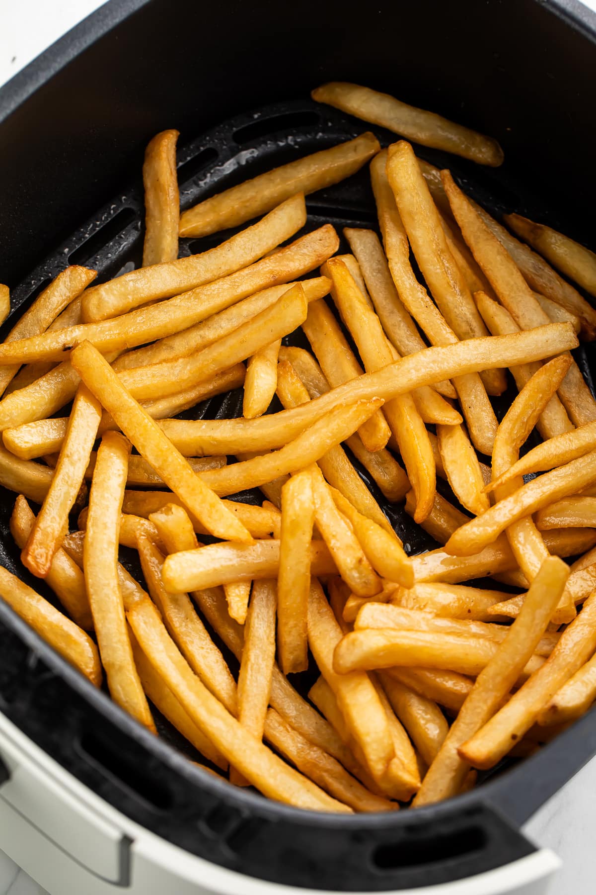 Reheated french fries in an air fryer basket.