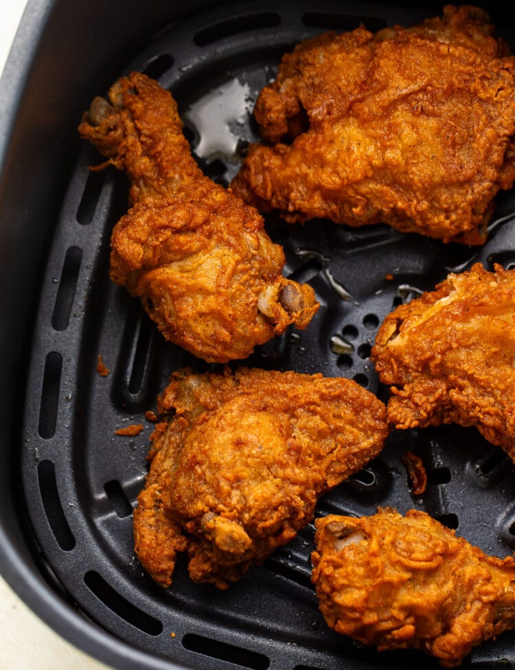 Crispy reheated fried chicken legs, thighs, and breasts in an air fryer basket.