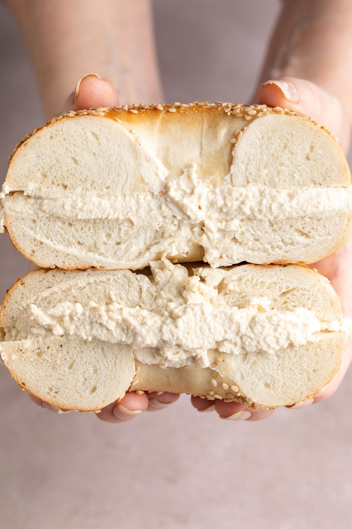 Thick layers of tofu cream cheese sandwiched between two bagel halves, stacked on top of each other.