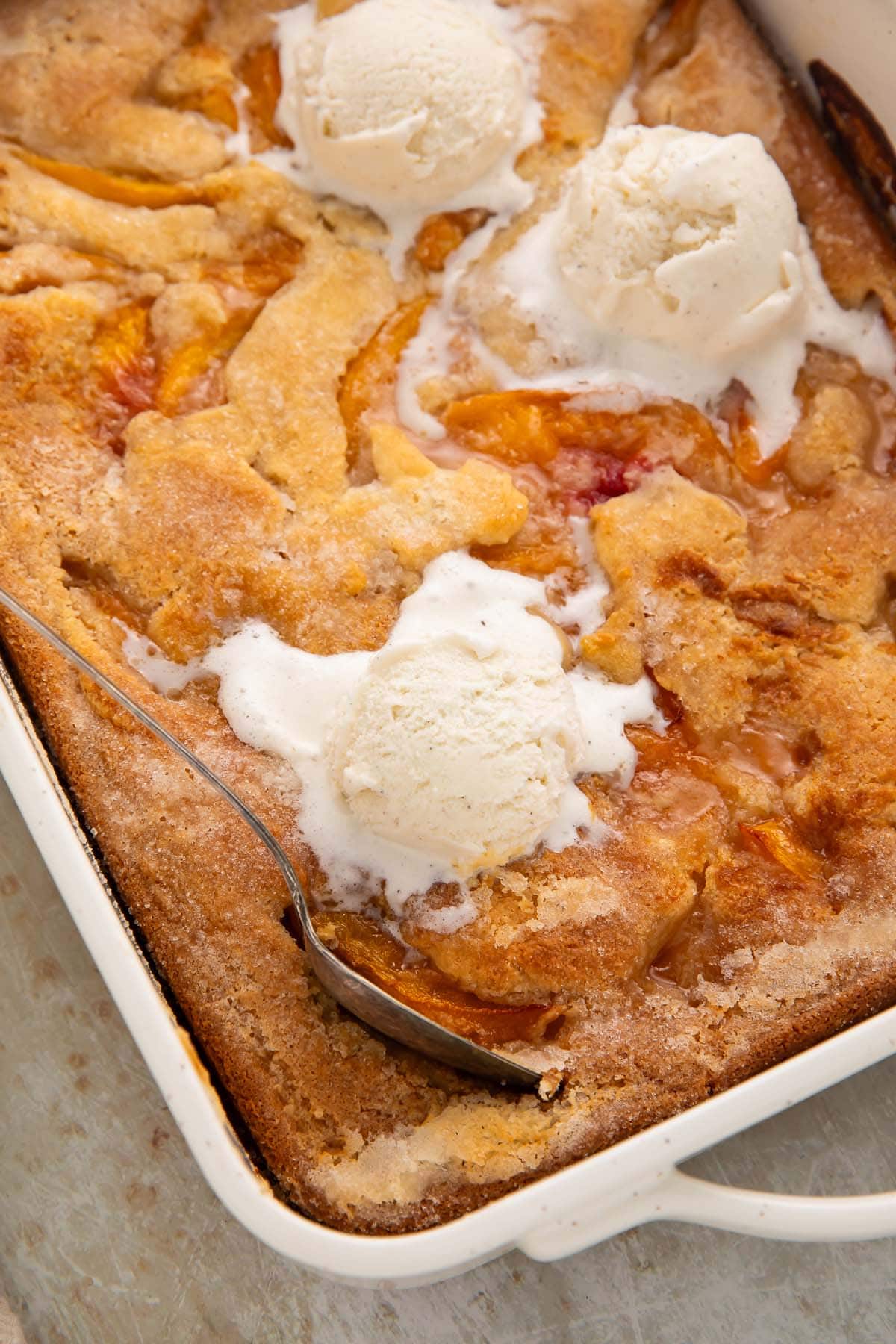 Overhead photo of a rectangular baking dish holding a gluten free peach cobbler topped with scoops of vanilla ice cream.