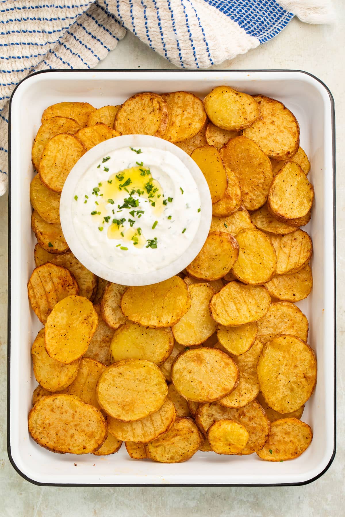 Thinly sliced potatoes, cooked in the air fryer, on a tray with a bowl of creamy dipping sauce.