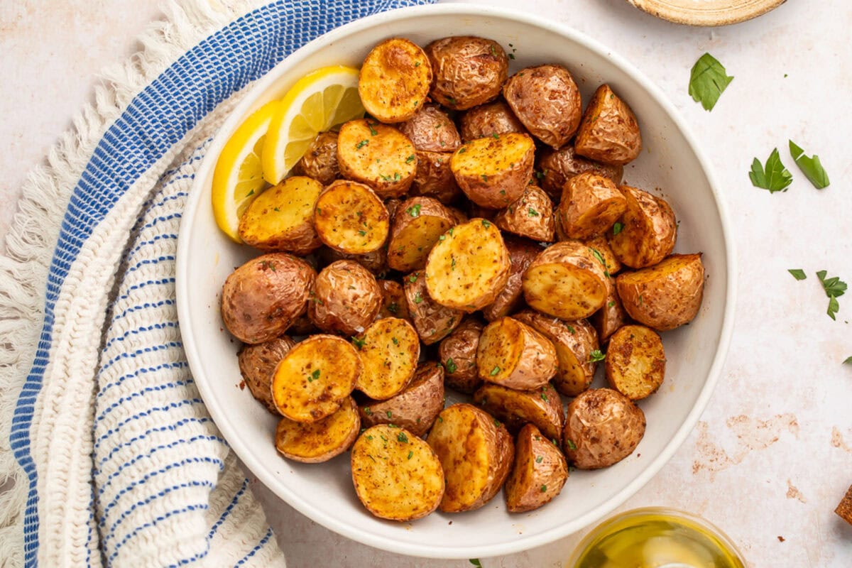 A bowl of air fryer red potatoes with 2 lemon slices next to a blue striped kitchen towel.