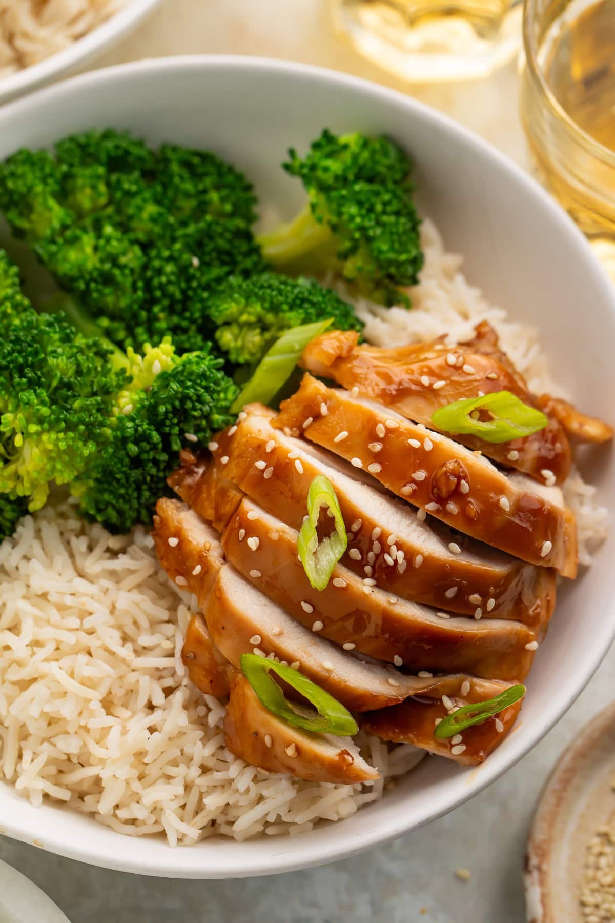 Sliced teriyaki chicken breast in a white bowl with brown rice and steamed broccoli.