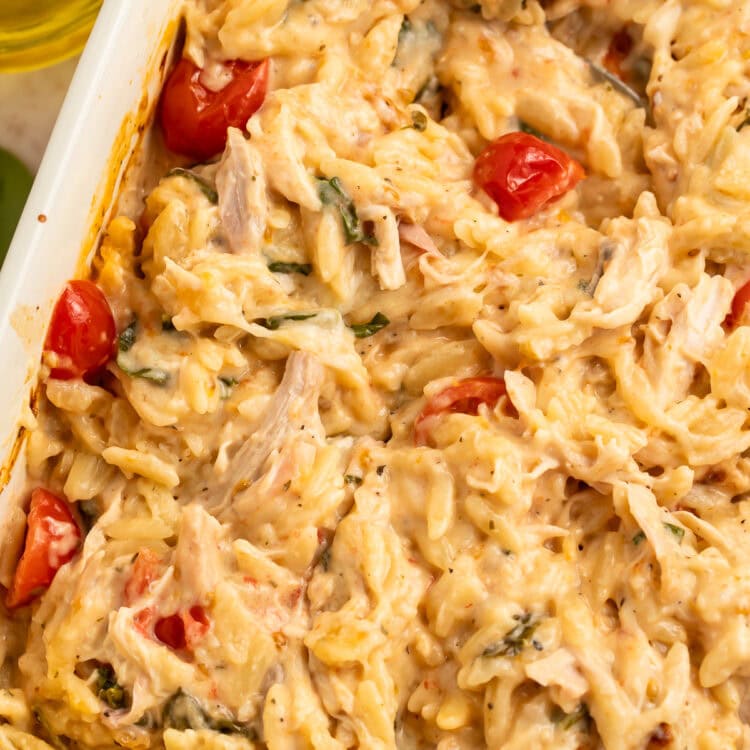 Close up of a stirred chicken and orzo bake in a white baking dish.