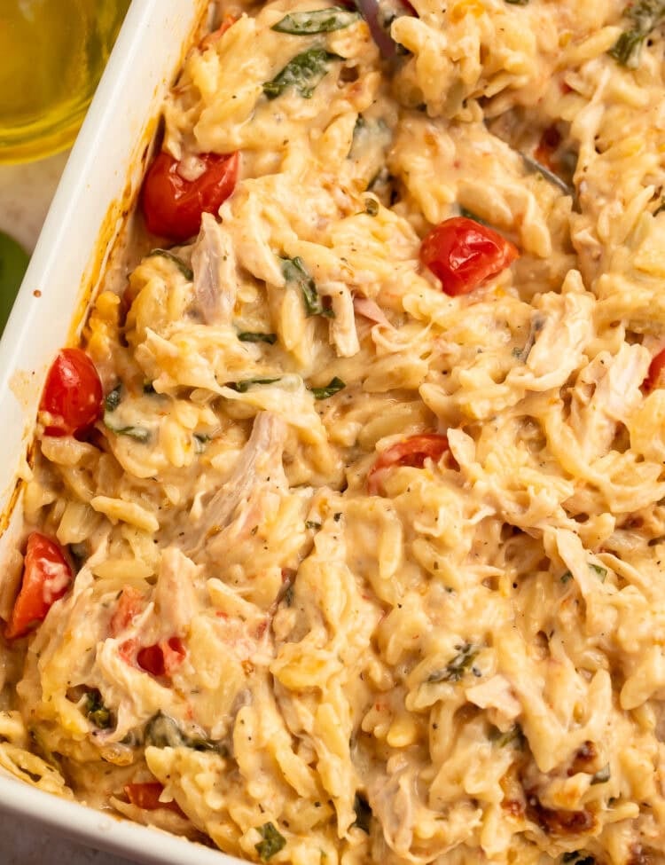 Close up of a stirred chicken and orzo bake in a white baking dish.