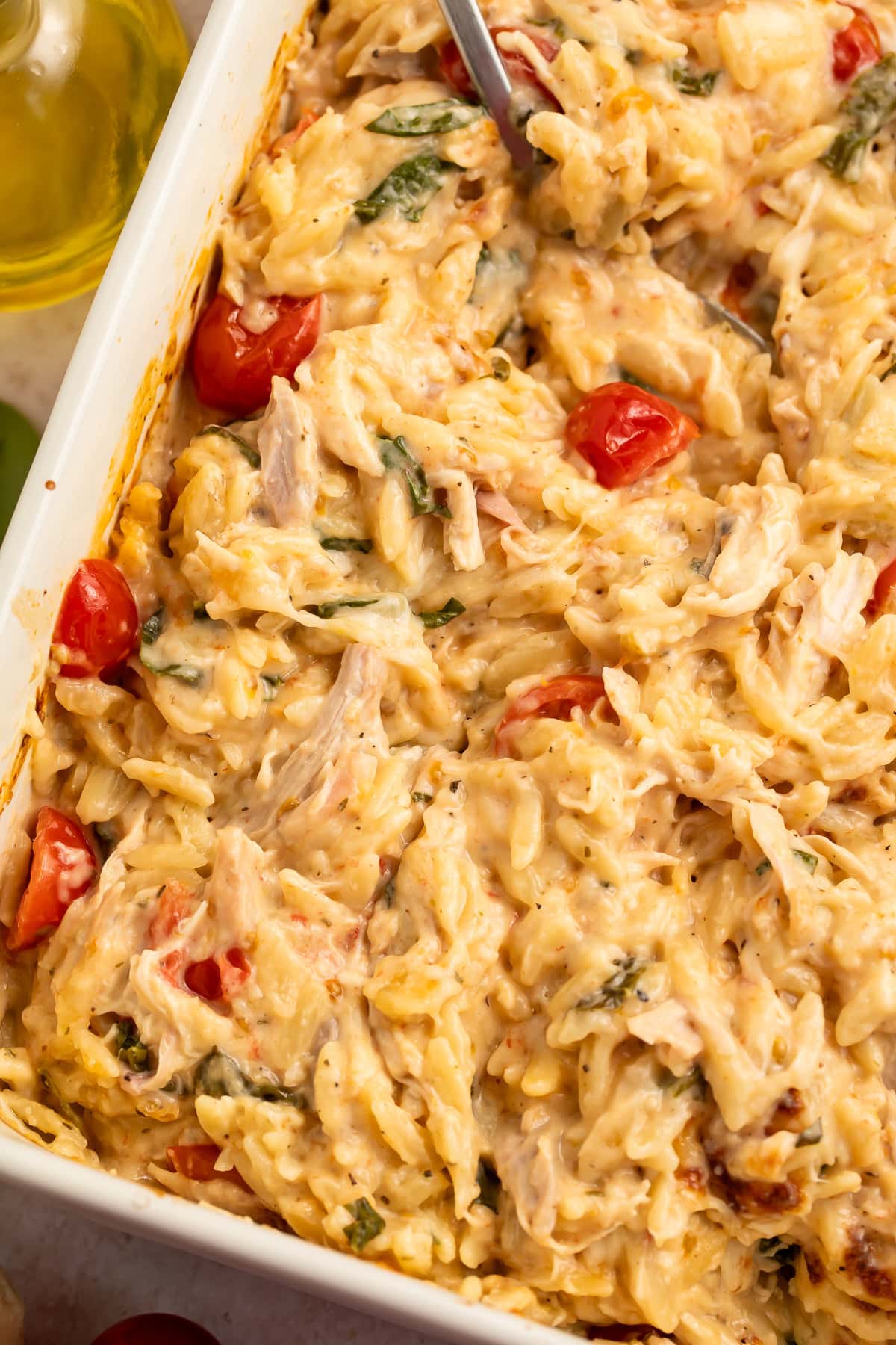 Close up of a stirred chicken and orzo bake in a white baking dish. 