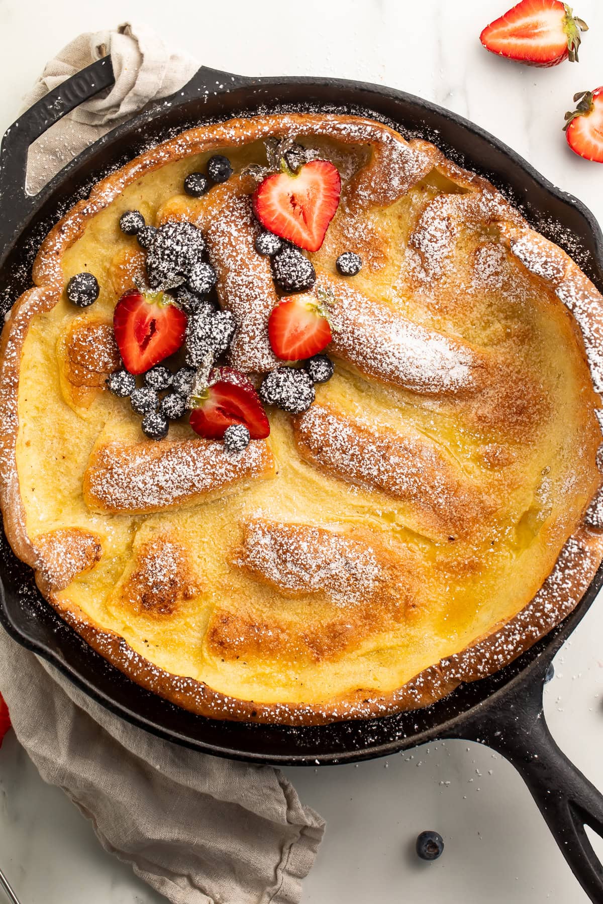 Dutch baby pancake in a cast iron skillet dusted with powdered sugar and topped with fresh berries.