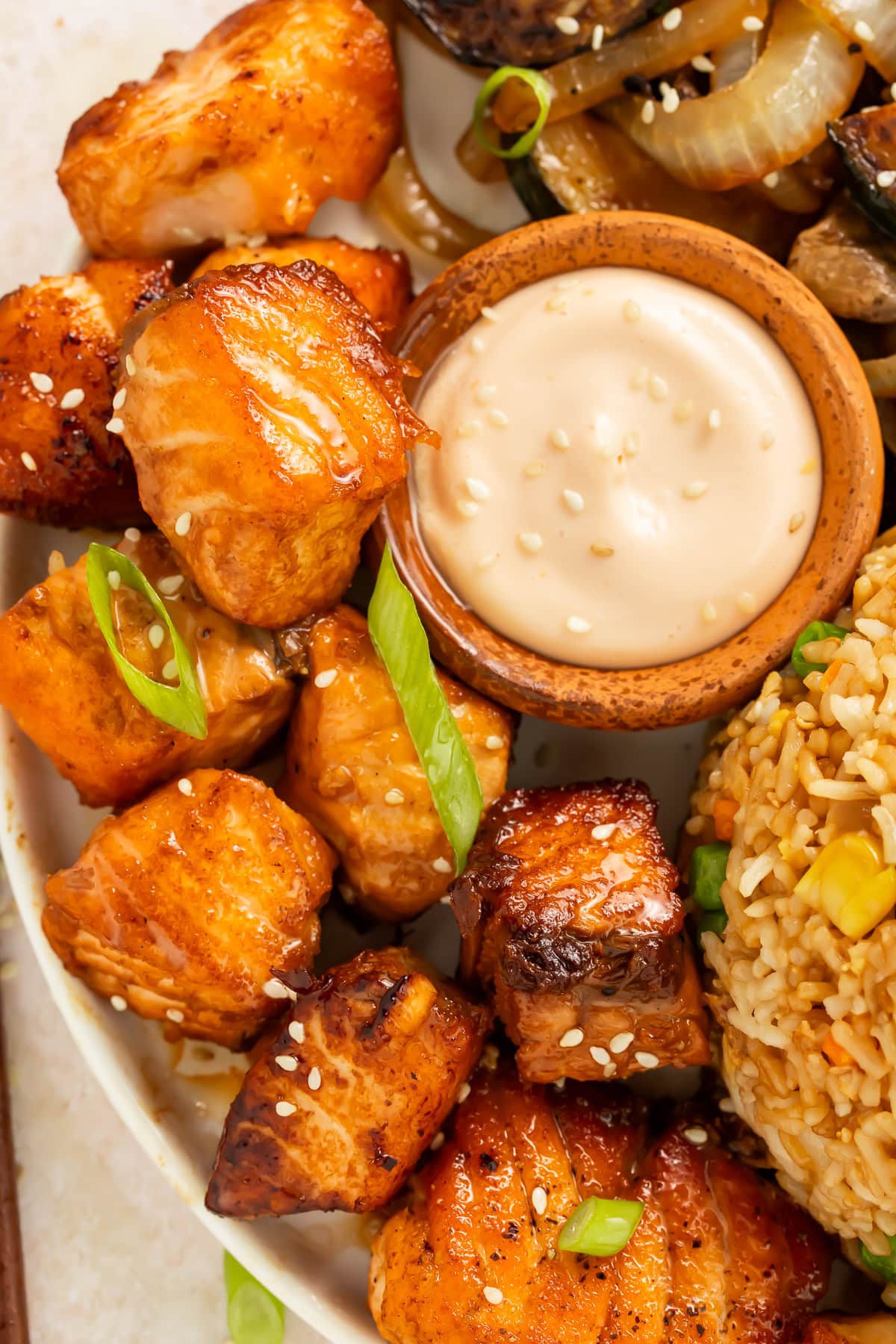 Close up of salmon hibachi bites on a plate with a pot of creamy dipping sauce.