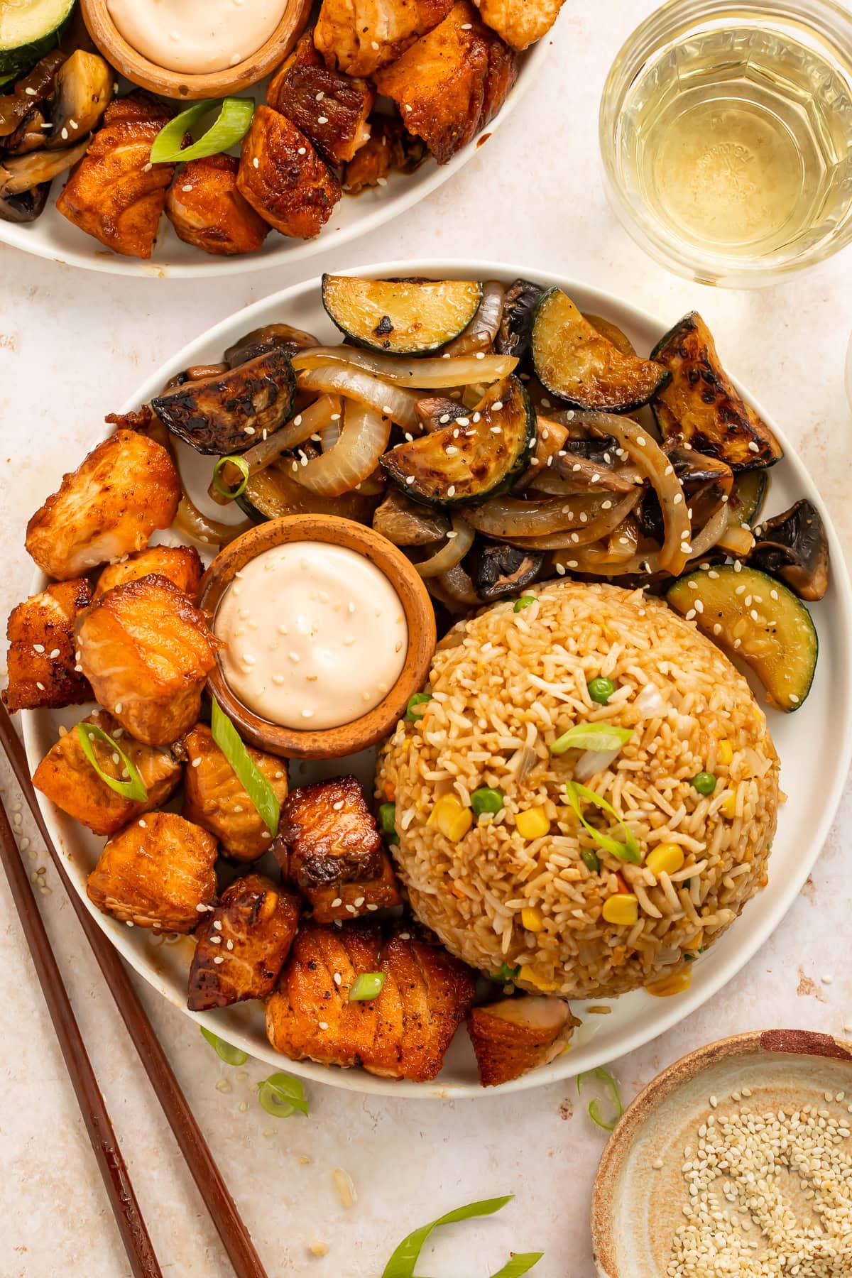 Bowl of hibachi salmon, mixed vegetables including mushroom, zucchini and onions, served with a mound of fried rice and a small wooden pot of creamy dipping sauce.