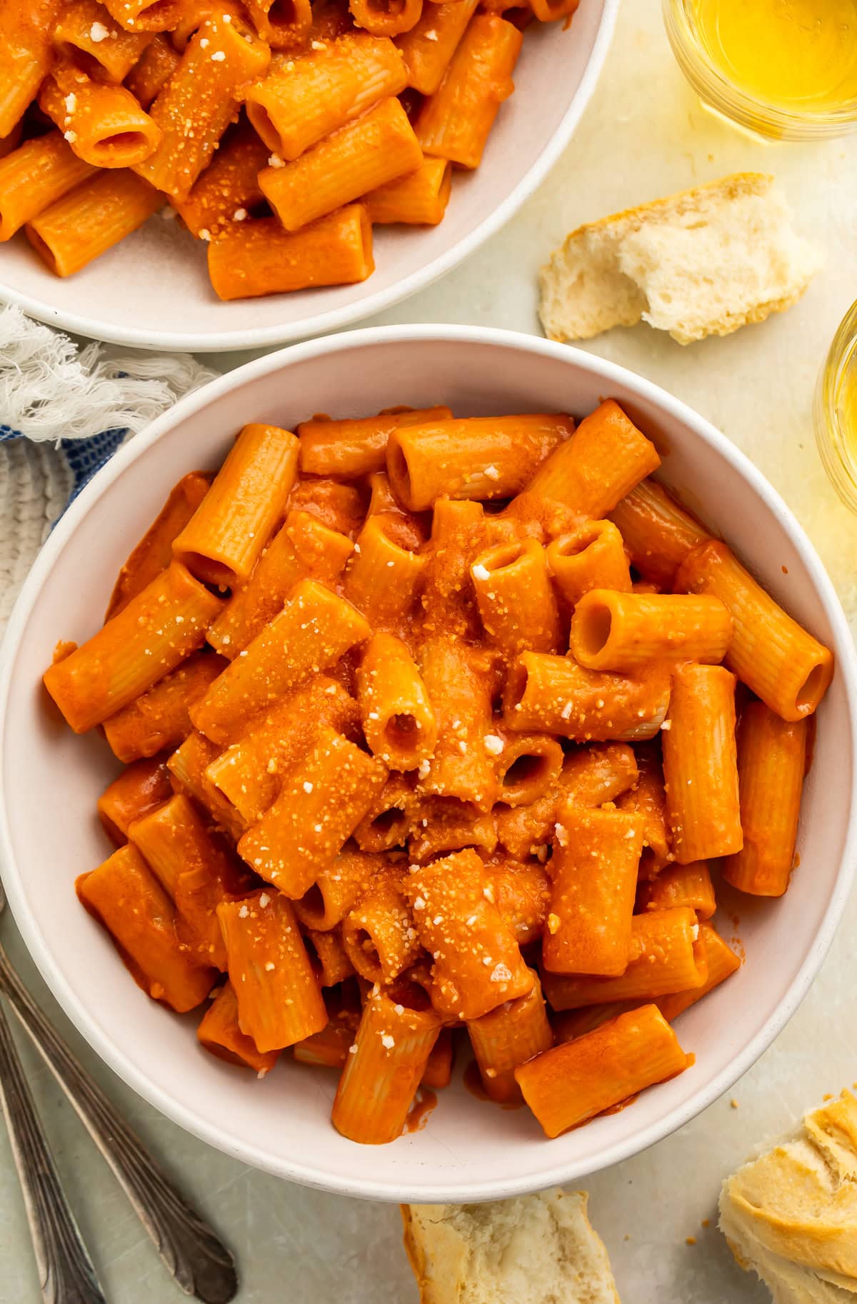 Bowl of vegan vodka pasta sauce tossed with rigatoni before being sprinkled with grated vegan parmesan.