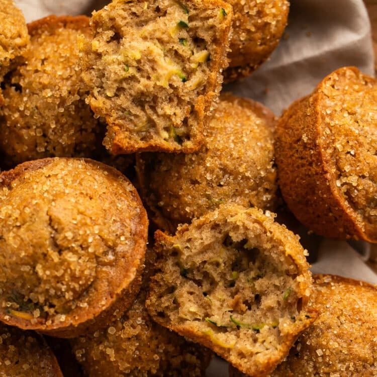Linen-lined basket of zucchini muffins, pictured close up with one torn in half.