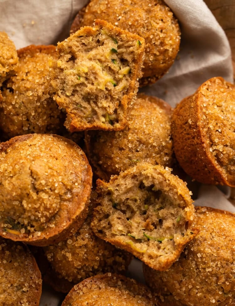 Linen-lined basket of zucchini muffins, pictured close up with one torn in half.