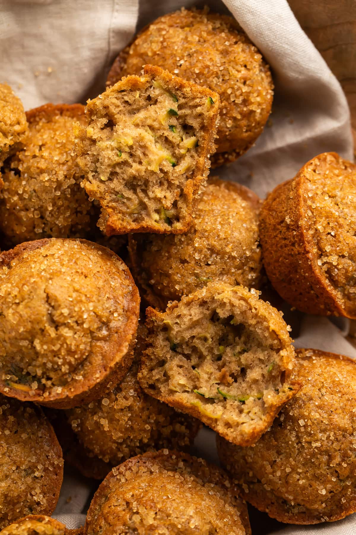 Linen-lined basket of zucchini muffins, pictured close up with one torn in half.