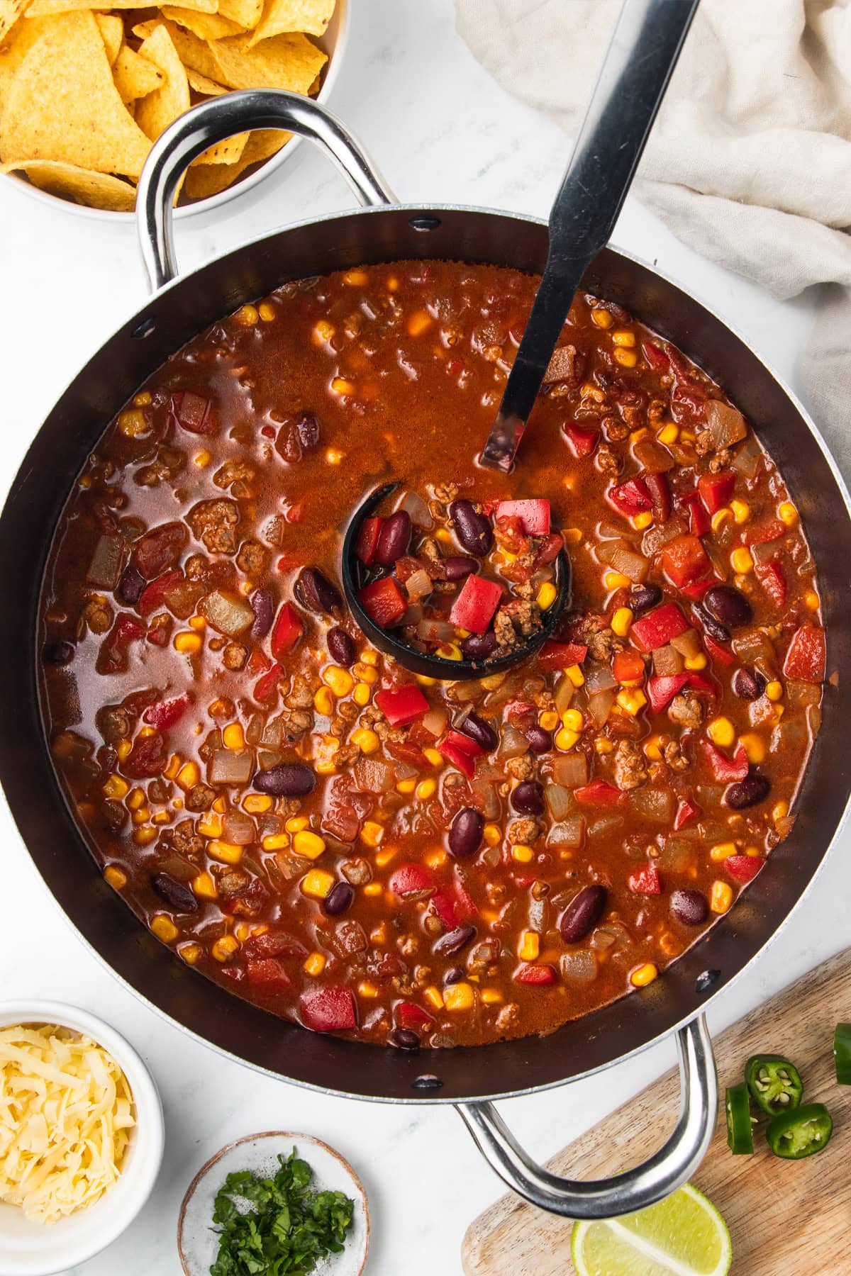 Chili with corn being ladled out of a big cooking pot.