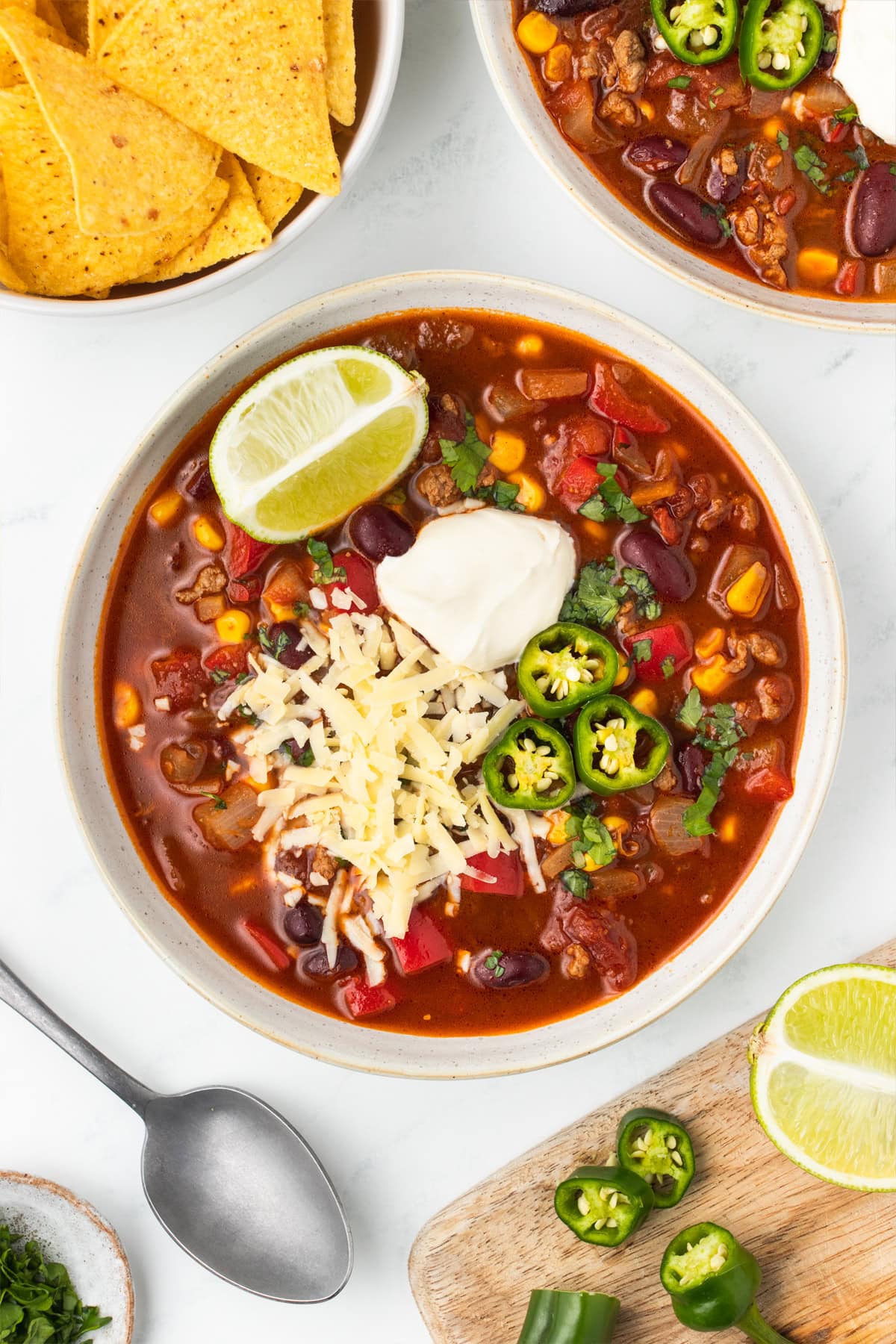 Bowl of chili topped with sour cream, shredded cheese, sliced jalapeños and a lime wedge.